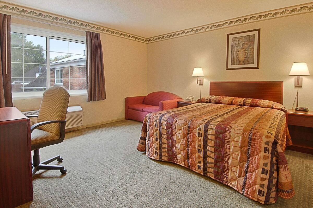 A hotel room with a bed, a desk, a chair, a couch, and two bedside lamps.