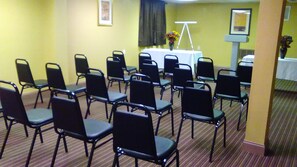 Conference room with a white table and black chairs, surrounded by a carpeted floor and framed artwork.
