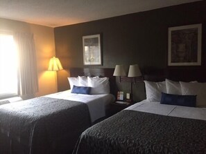 A hotel room with two beds, a nightstand, a lamp, and a painting on the wall. - Days Inn by Wyndham Cleveland Lakewood (Lakewood)