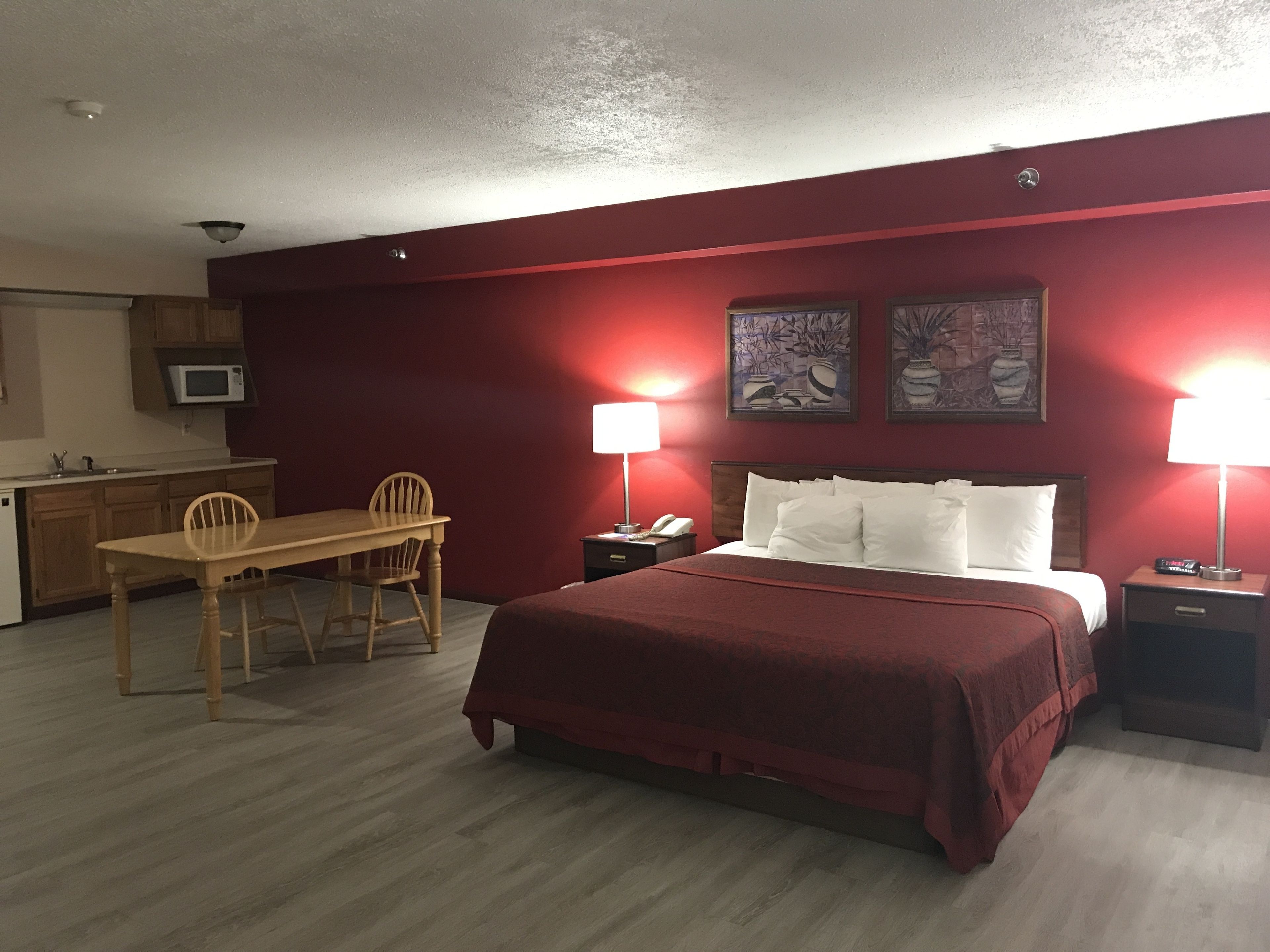 Habitación de hotel con cama, mesitas de noche, un escritorio con silla, microondas y obras de arte en las paredes.