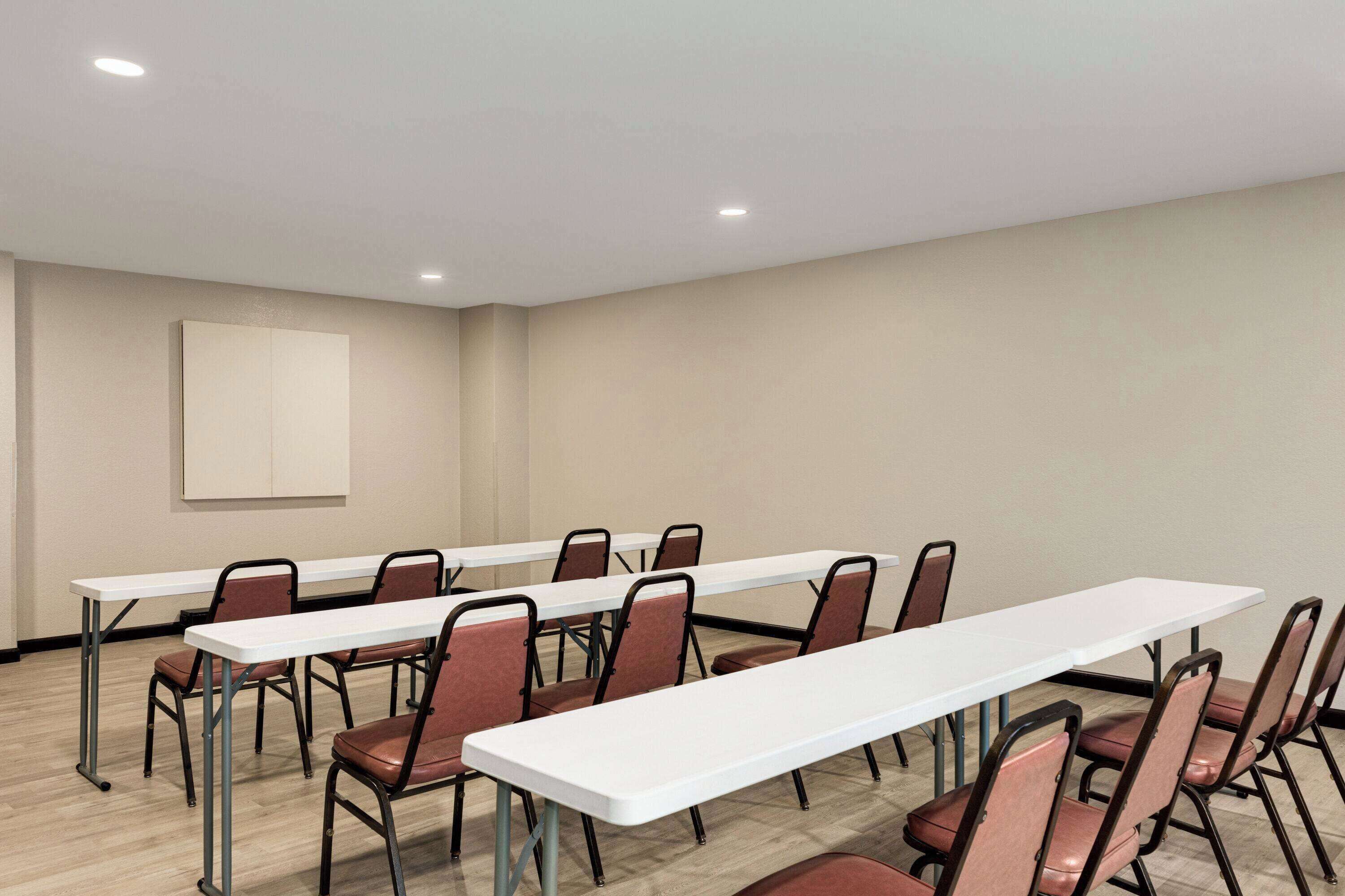 A conference room with long tables and chairs, a neutral wall, and recessed ceiling lights.