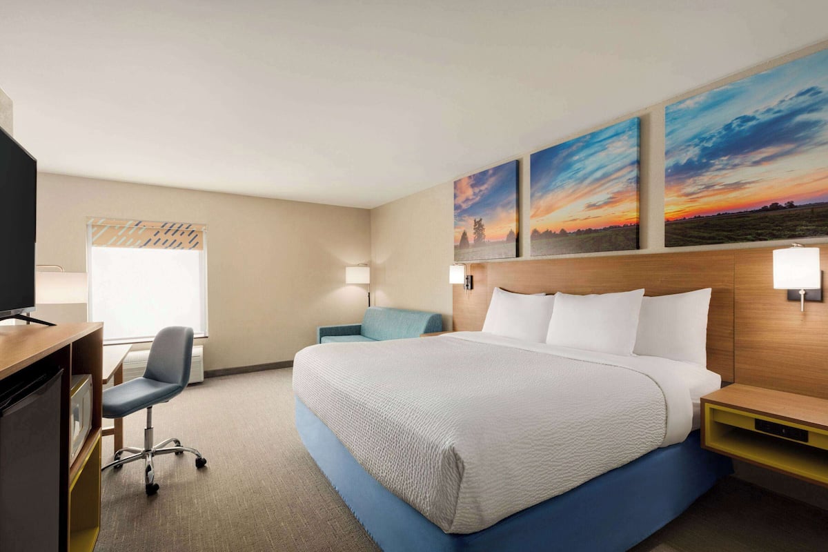 A hotel room with a large bed, a desk with a chair, a television, and two wall-mounted lamps.