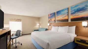 A hotel room with a large bed, a desk with a chair, a television, and two wall-mounted lamps.