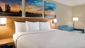 A hotel room with a large bed, two wall-mounted paintings, a nightstand, a bedside lamp, and a chair. - Days Inn by Wyndham Hillsboro (Hillsboro)