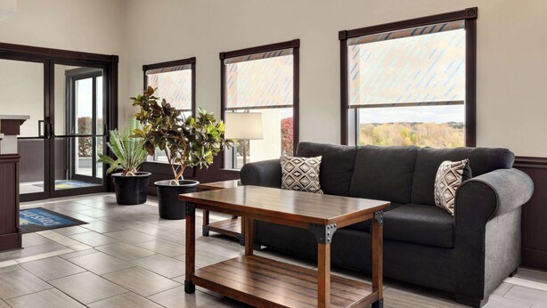 A modern living room with a dark gray sofa, a wooden coffee table, and potted plants. - Days Inn by Wyndham Hillsboro (Hillsboro)