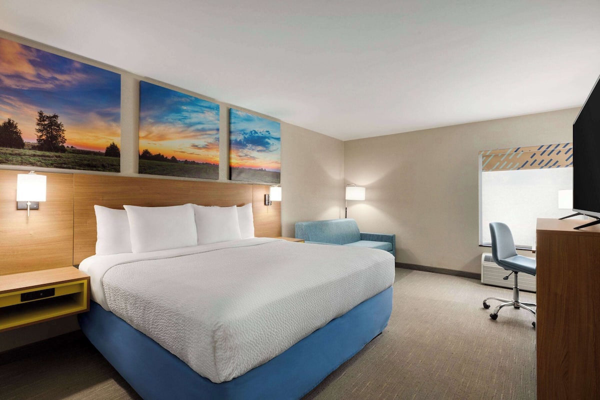 A hotel room with a large bed, a desk, a chair, and two wall-mounted lamps.