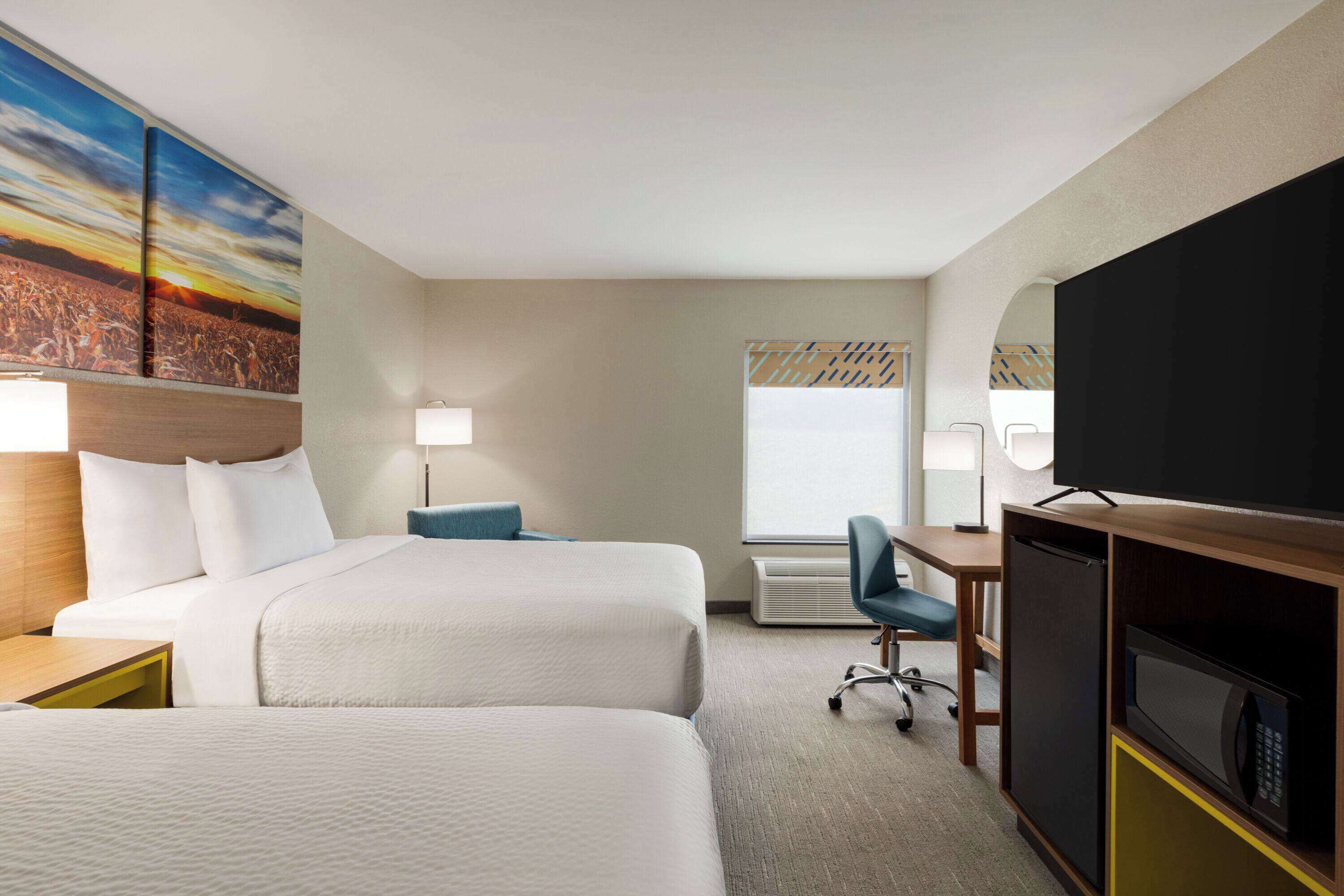 Une chambre d’hôtel avec deux lits, un bureau, une télévision et une grande fenêtre.