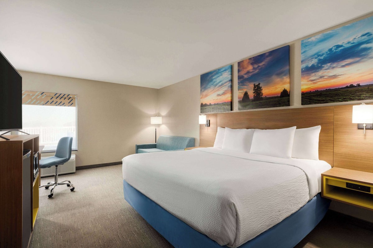 A hotel room with a large bed, a desk, a chair, and a TV.