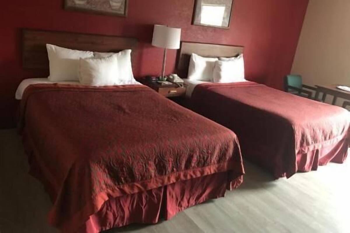 A hotel room with two beds, a nightstand, a lamp, and two framed pictures on the wall.