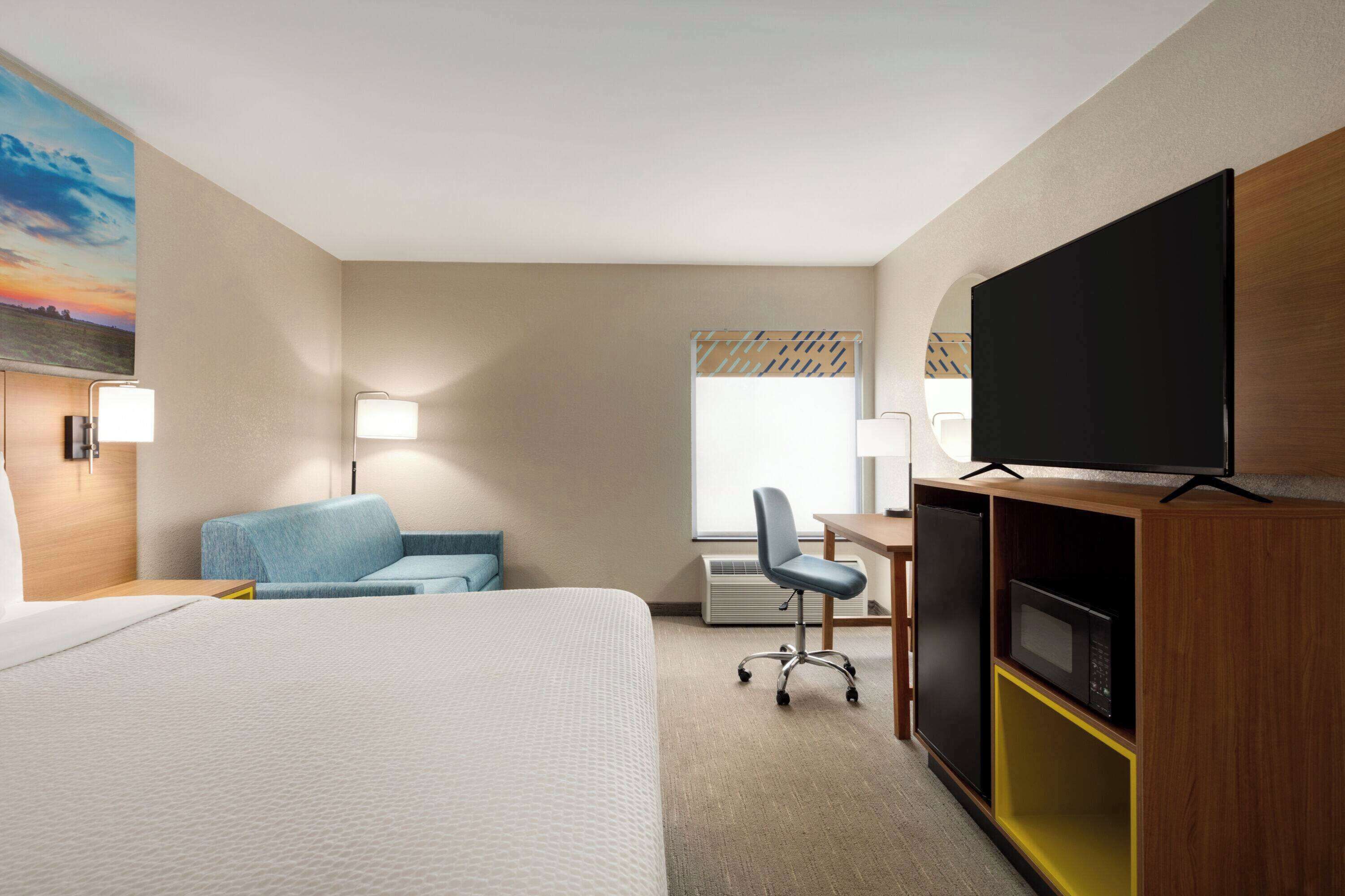 A hotel room with a bed, a desk with a flat-screen TV, a chair, a sofa, and a microwave.