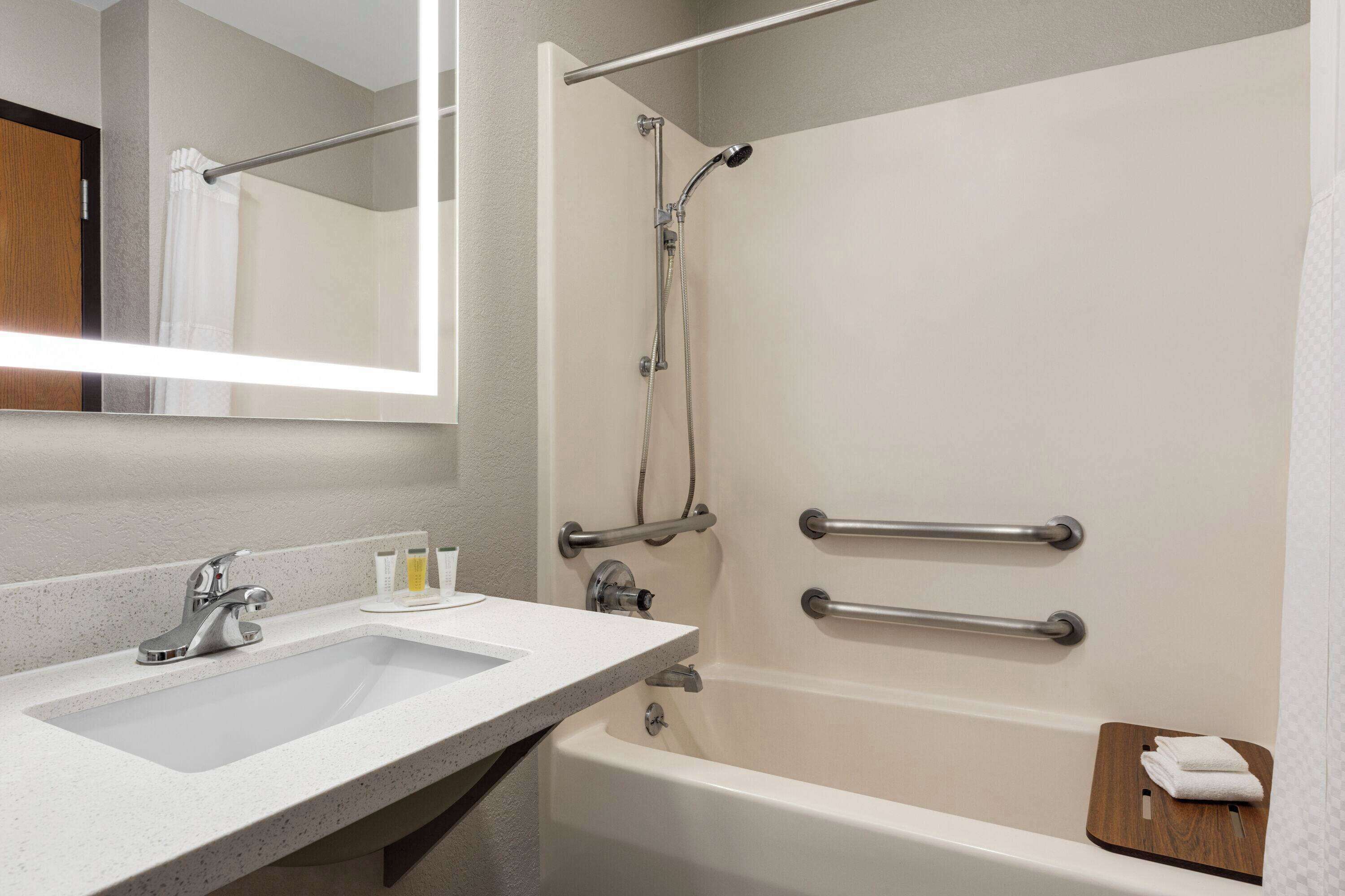Baño con lavamanos, espejo, ducha y barras de apoyo.