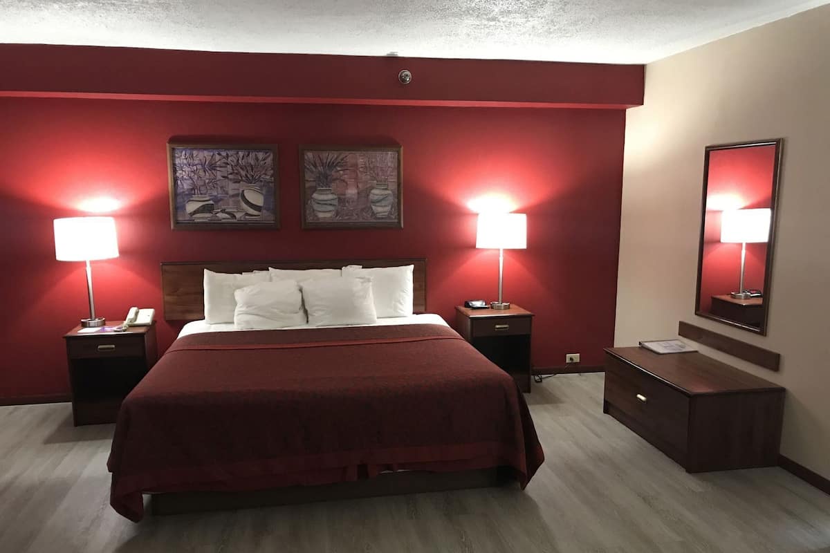 A hotel room with a large bed, two bedside lamps, a nightstand, a dresser, and two framed artworks on the wall.