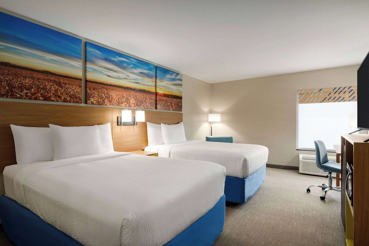A hotel room with two beds, a desk, and a large painting on the wall.