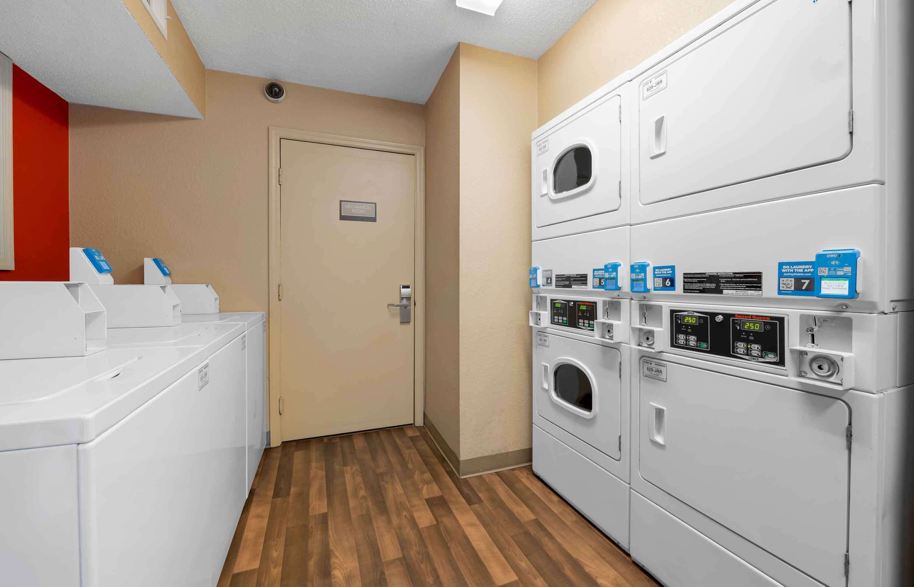 A laundry area with multiple washing machines and dryers, a door with a sign, and a wooden floor.