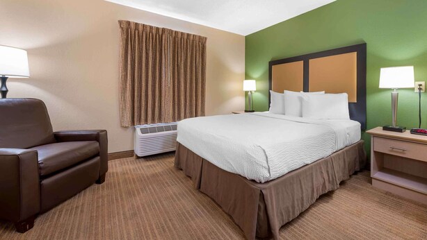 Quarto de hotel com cama, cadeira, luminária, aquecedor e parede verde.