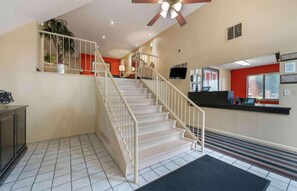 A hotel lobby with a staircase, a reception desk, and a ceiling fan. - Studio 6 Extended Stay Fairfield, OH - Cincinnati (Fairfield)