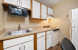 A compact kitchen with a microwave, stove, sink, and white cabinets. - Studio 6 Extended Stay Fairfield, OH - Cincinnati (Fairfield)