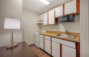 Una cocina compacta equipada con microondas, estufa, lavabo y una lámpara.