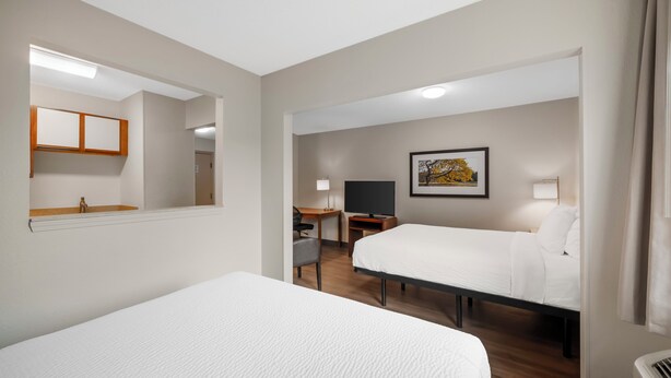 Habitación de hotel con dos camas, un escritorio, una silla, un televisor y un cuadro en la pared.