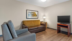 Una sala de estar con un sofá marrón, un sillón gris, un mueble de televisión de madera y un cuadro en la pared.