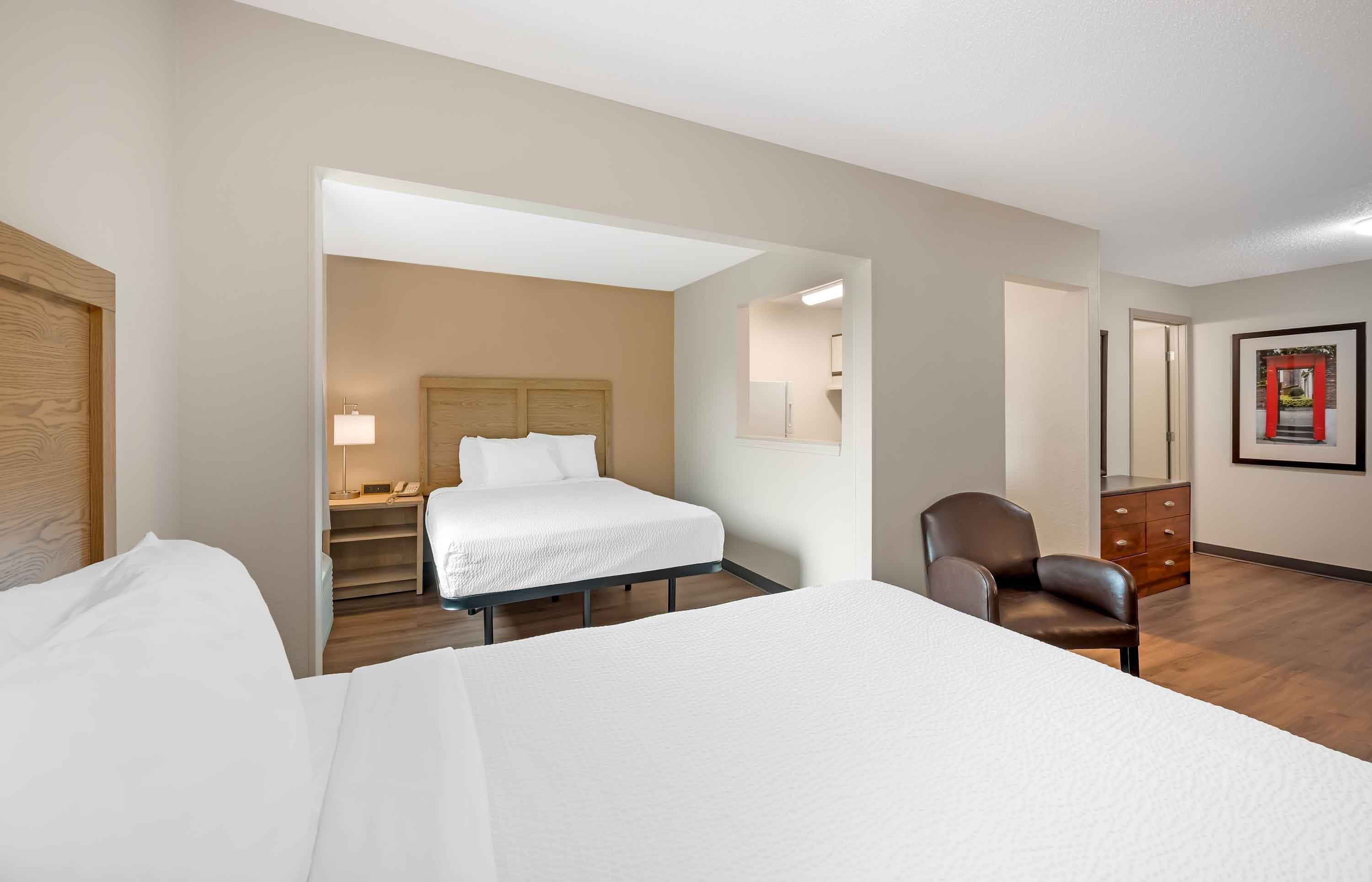 Una habitación de hotel con cama, una silla, una mesita de noche, una lámpara y un aparador.