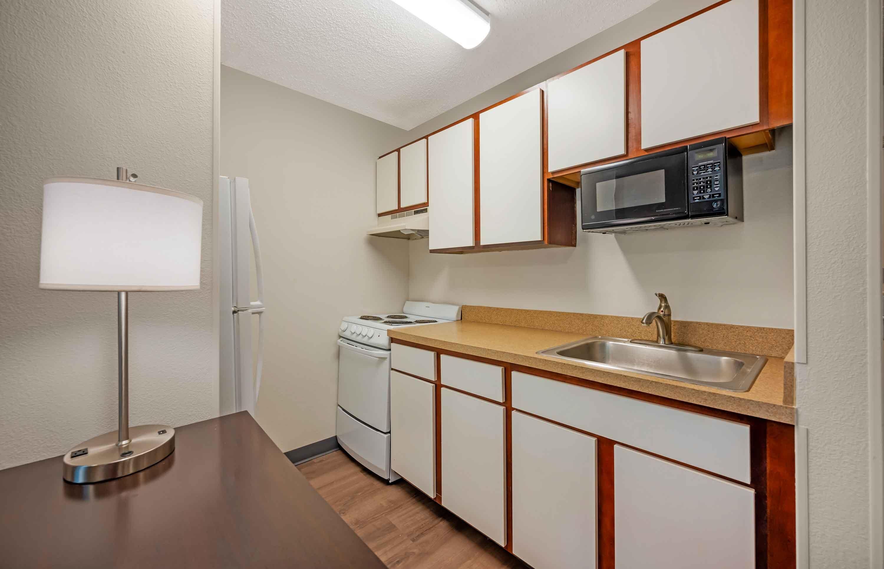 A compact kitchen with a stove, microwave, sink, and a lamp.