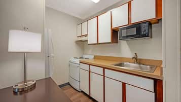 A compact kitchen with a stove, microwave, sink, and a lamp.