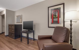 Habitación de hotel con televisión de pantalla plana, un sillón de cuero marrón, escritorio con lámpara, cómoda y cuadros en las paredes.