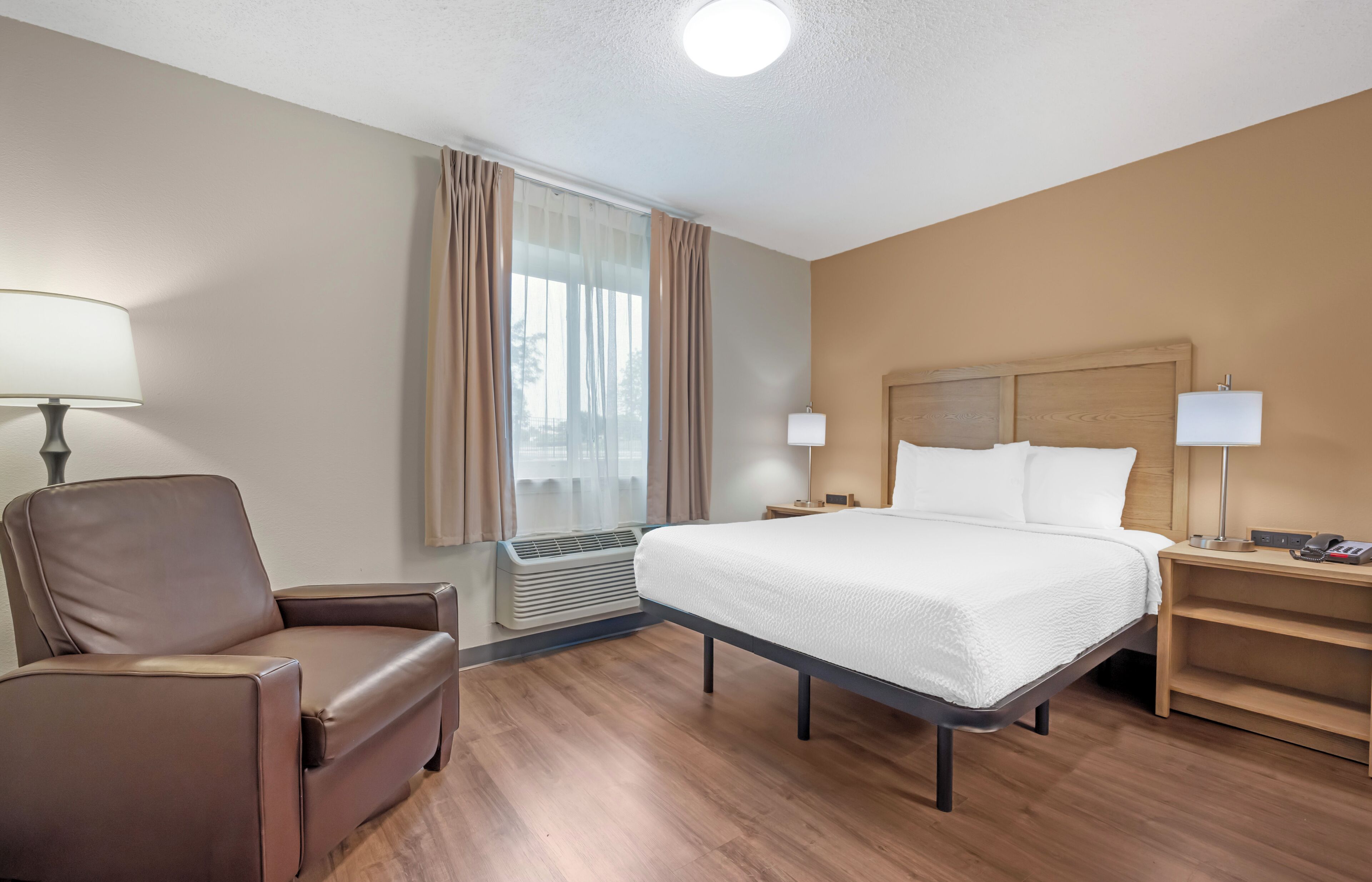 A hotel room with a bed, a chair, a desk, a lamp, and a window with curtains.