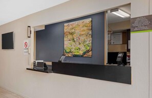 A hotel reception desk with a painting, a no smoking sign, a phone, and a digital display.