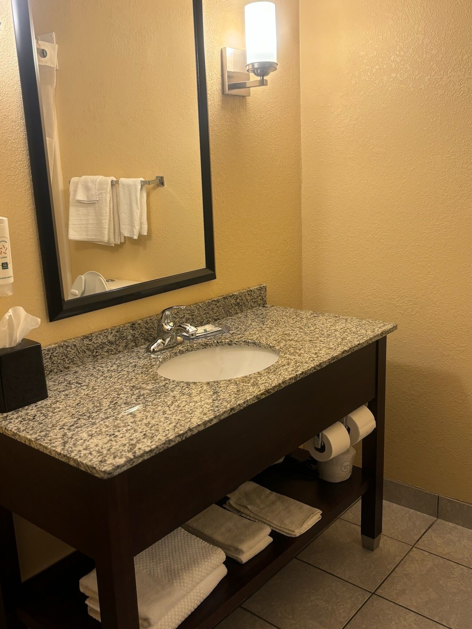 A bathroom with a granite countertop sink, a mirror, and a towel rack.