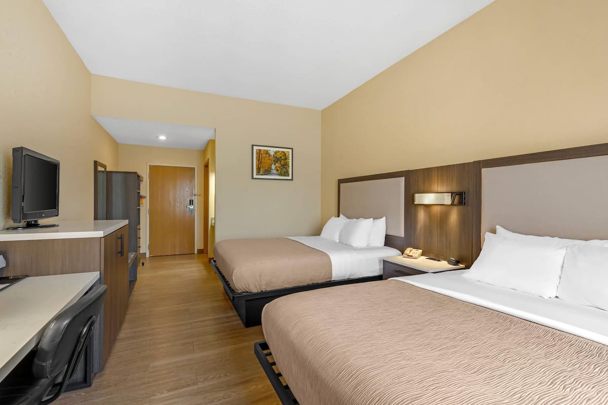 Une chambre d’hôtel avec deux lits, un bureau avec un ordinateur, une télévision et une porte donnant sur une autre pièce.