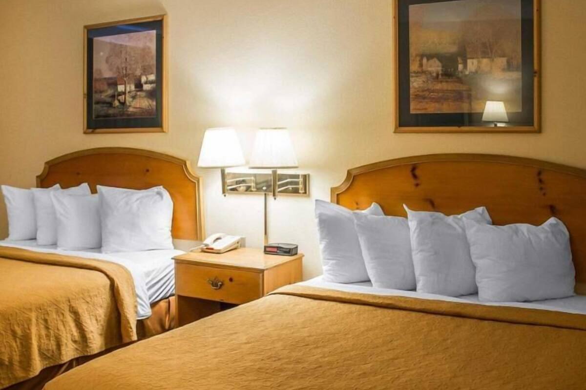 A hotel room with two beds, a nightstand with a lamp, and two framed pictures on the walls.