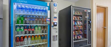 Two vending machines, one with a blue exterior and the other black, both stocked with beverages and snacks.