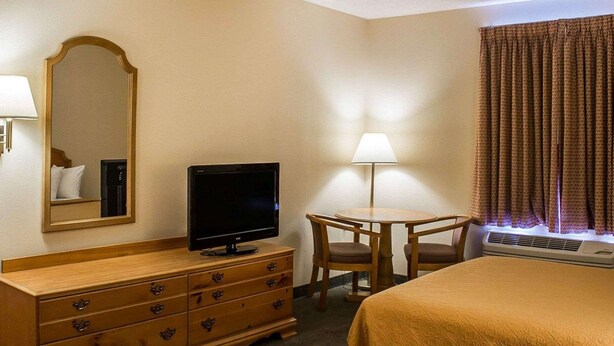 A hotel room with a bed, a TV on a dresser, a desk with a lamp, and a window with curtains. - Quality Inn & Suites Bellville - Mansfield (Bellville)