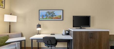A hotel room with a sofa, desk, chair, TV, and a framed picture on the wall.