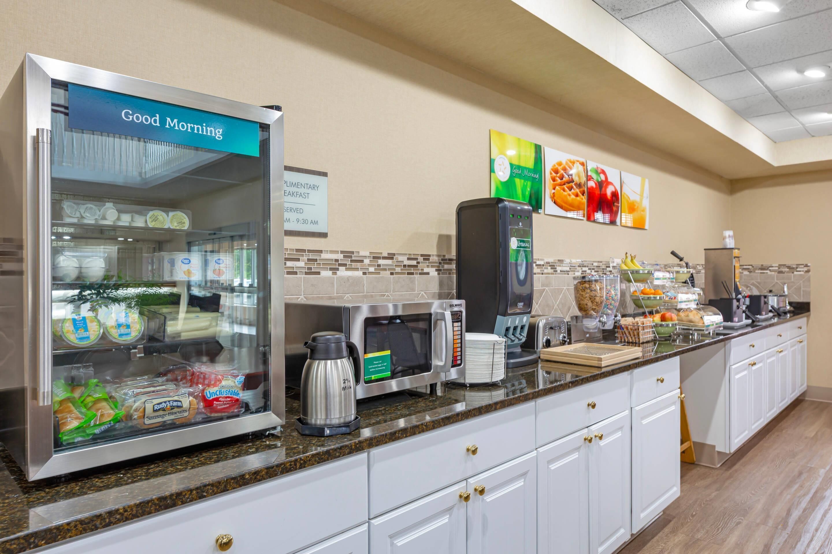 A breakfast bar with a refrigerator, microwave, coffee maker, and various food items.