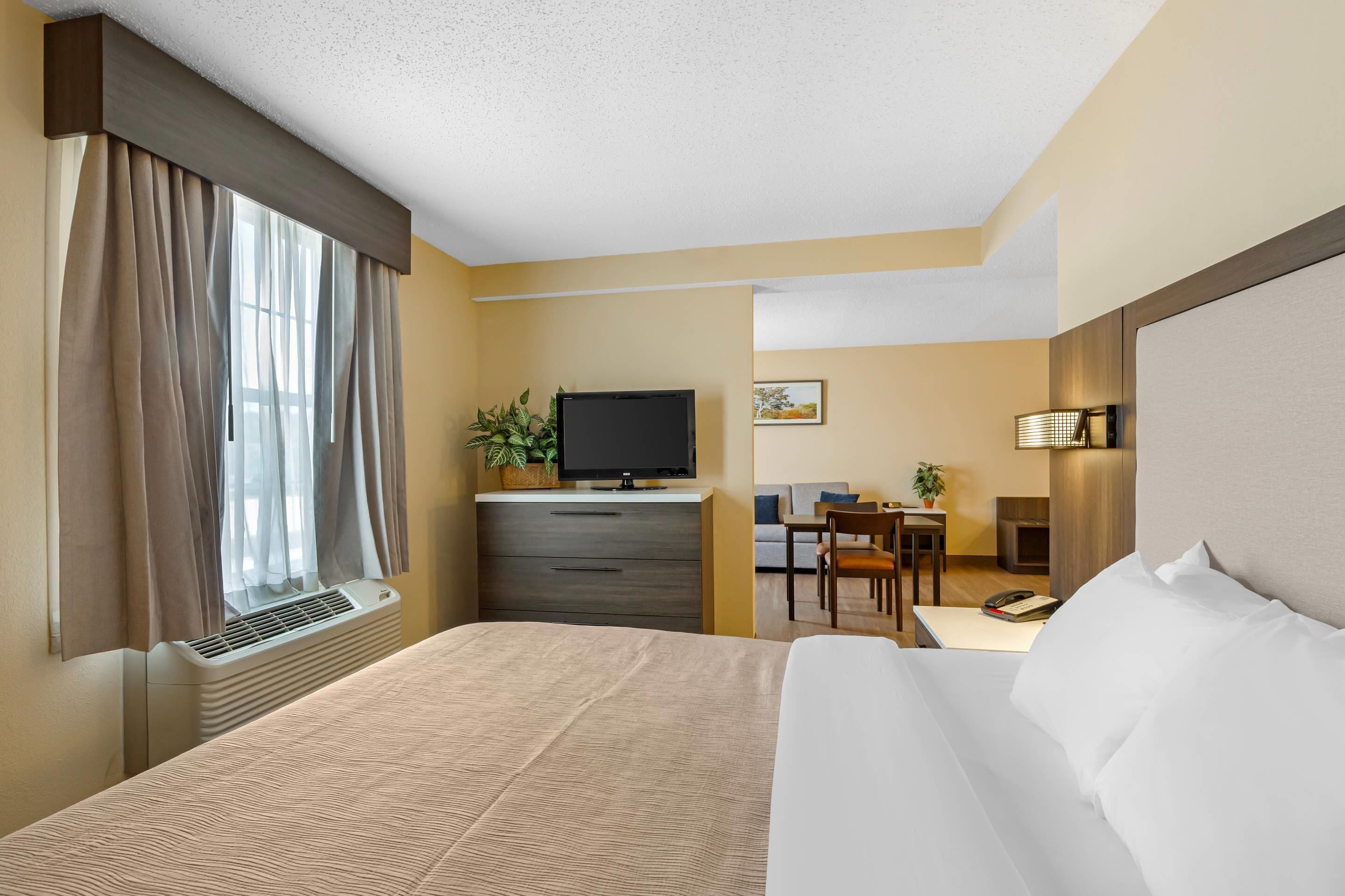 A hotel room with a bed, a desk, a television, and a window with curtains.