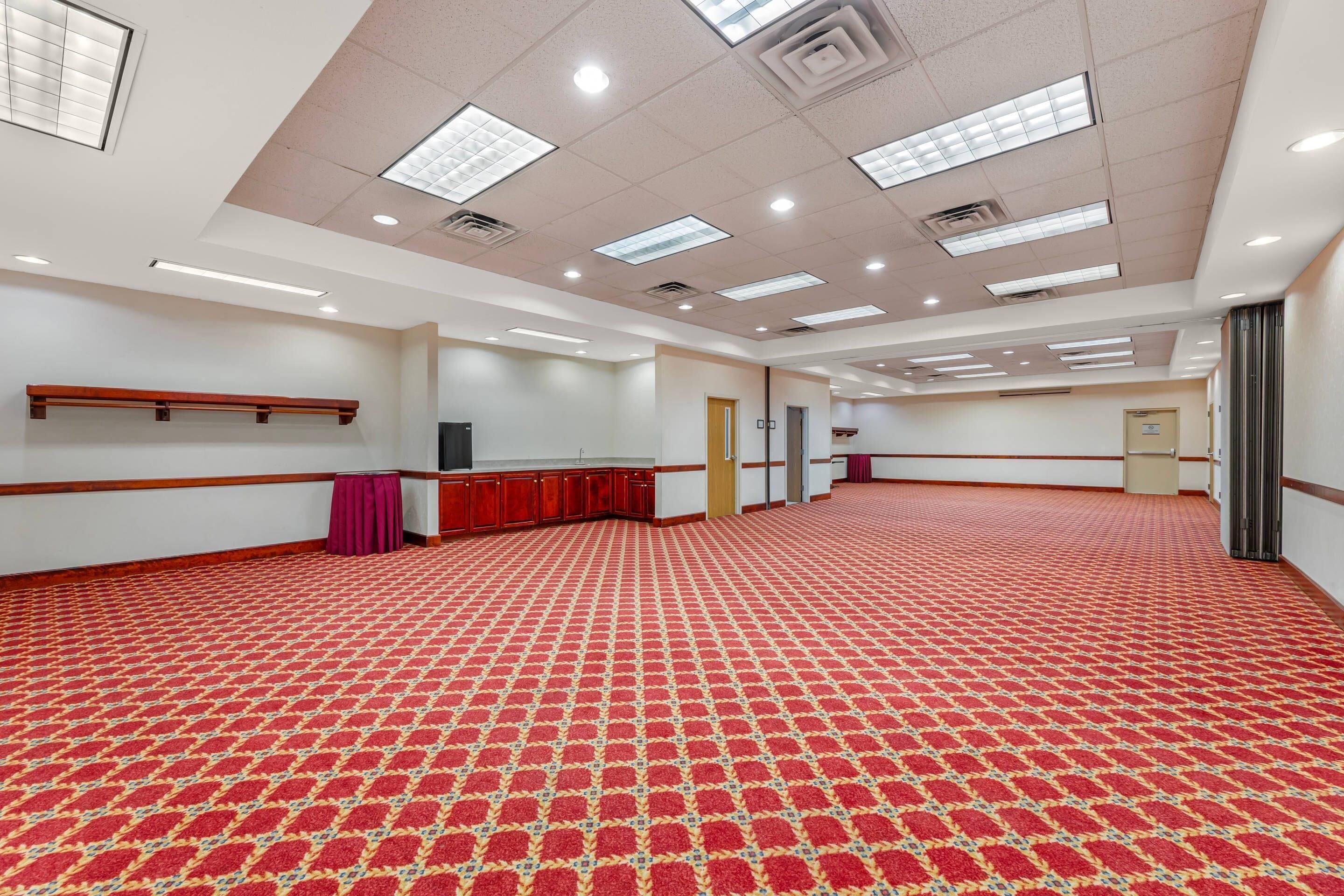 A large, well-lit room with a patterned carpet, a wooden bench, and a door.