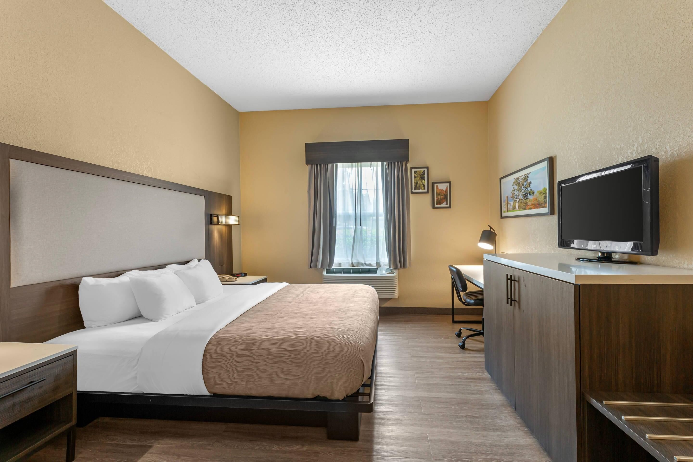 Une chambre d’hôtel équipée d’un lit, d’un bureau, d’une télévision et d’une fenêtre avec des rideaux.