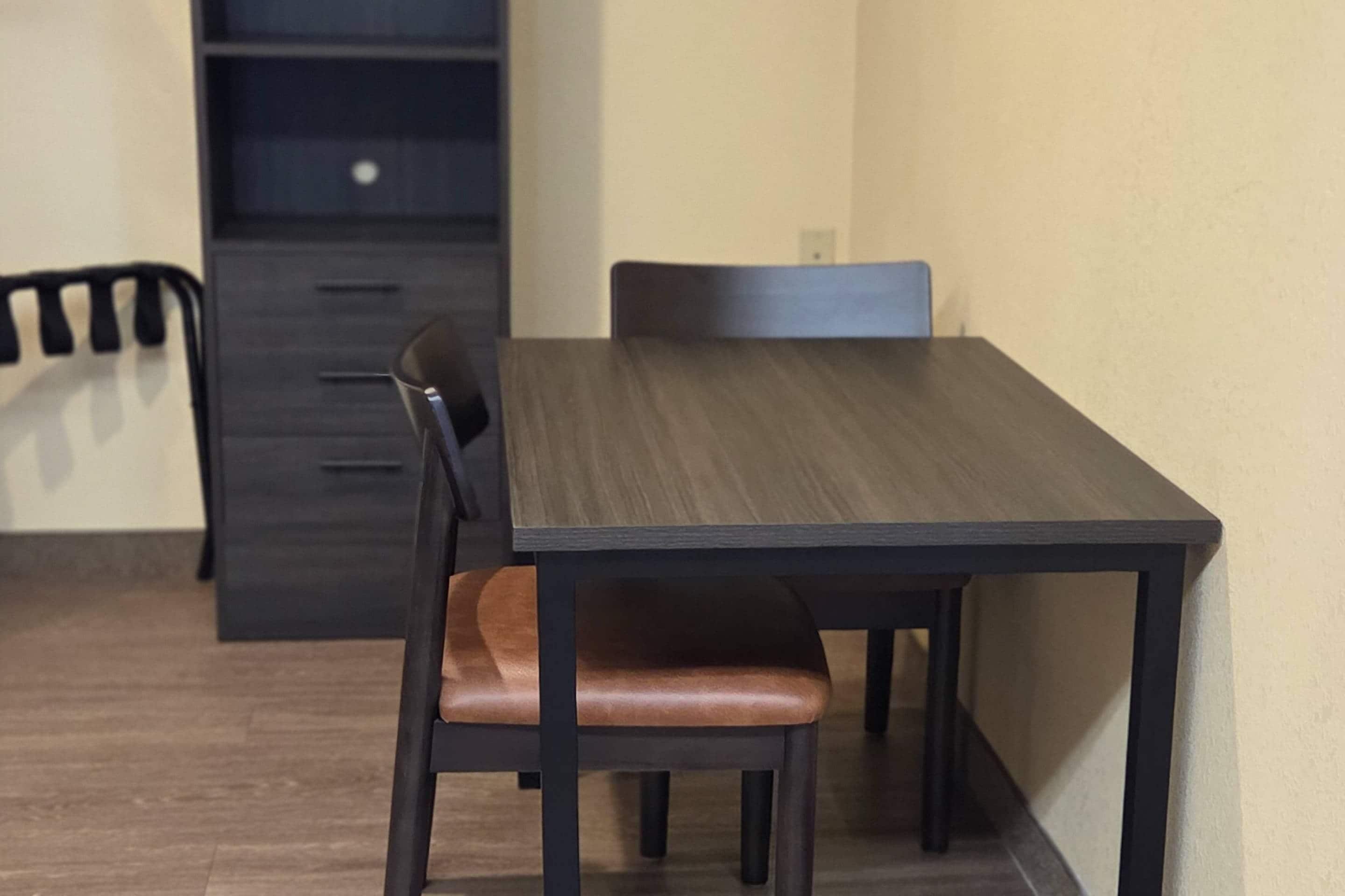 A dining area with a dark wooden table and chairs, a light-colored wall, and a dark cabinet in the background.