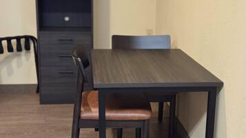 A dining area with a dark wooden table and chairs, a light-colored wall, and a dark cabinet in the background.