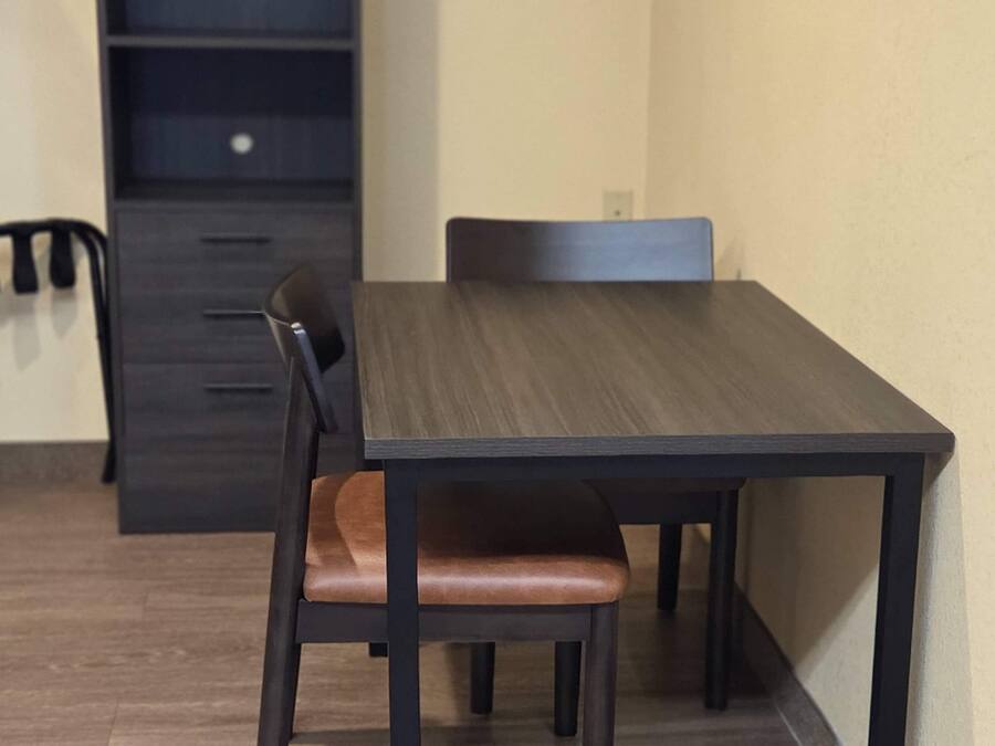 A dining area with a dark wooden table and chairs, a light-colored wall, and a dark cabinet in the background.