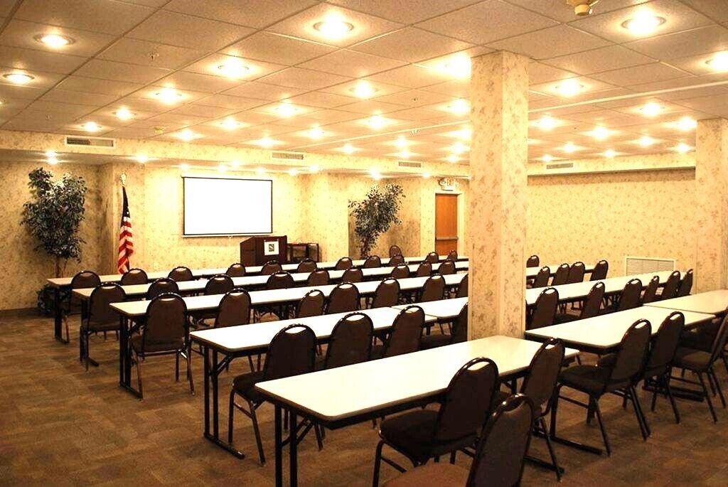 A conference room with rows of tables and chairs, a projector screen, and an American flag.