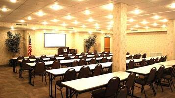 Un salón de conferencias con filas de mesas y sillas, una pantalla de proyector y una bandera estadounidense.