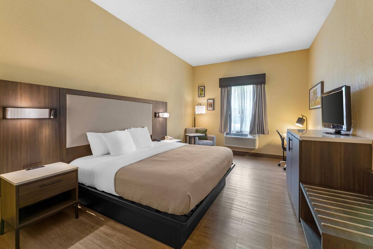 A hotel room with a bed, bedside tables, a desk, a television, and a window with curtains.