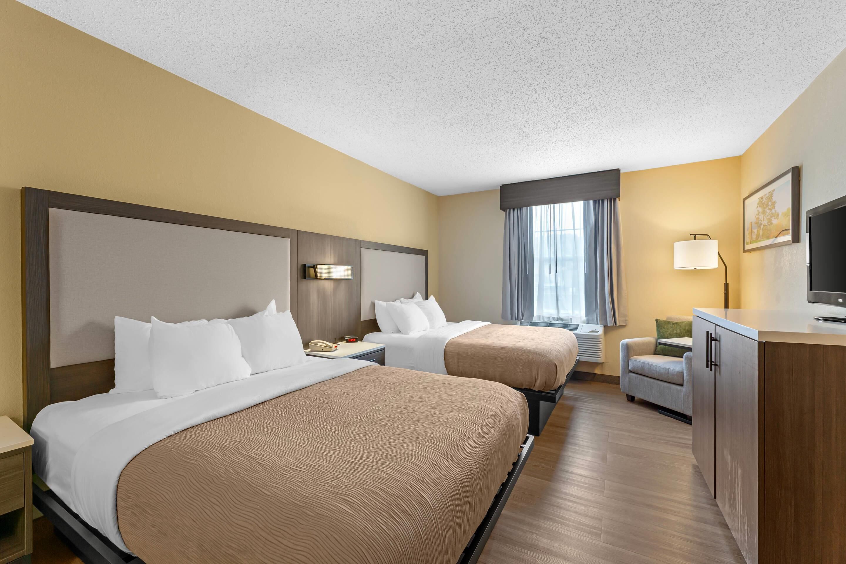 A hotel room with two beds, a desk, a chair, a TV, and a window with curtains.