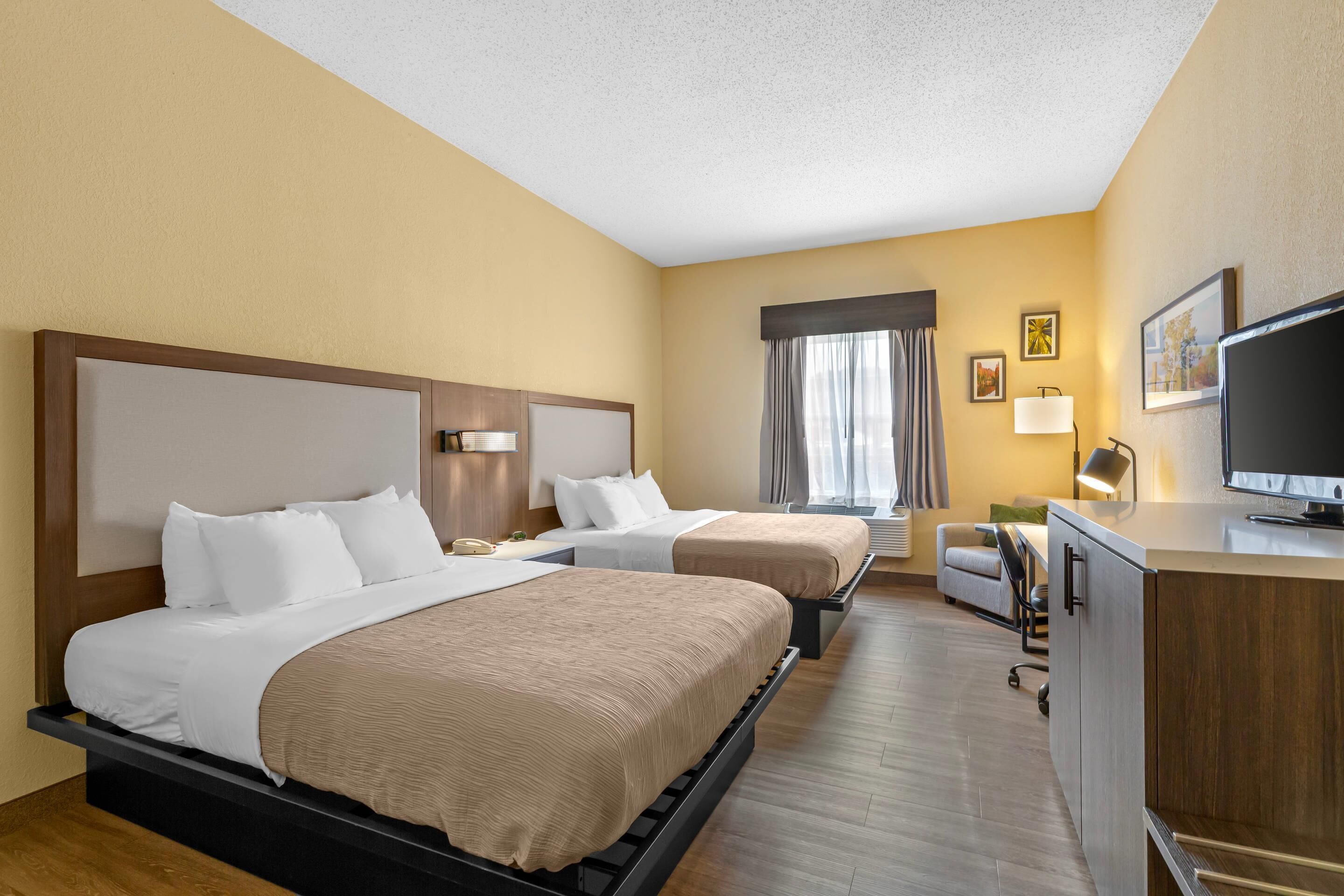 A hotel room with two beds, a desk, a television, and a window with curtains.