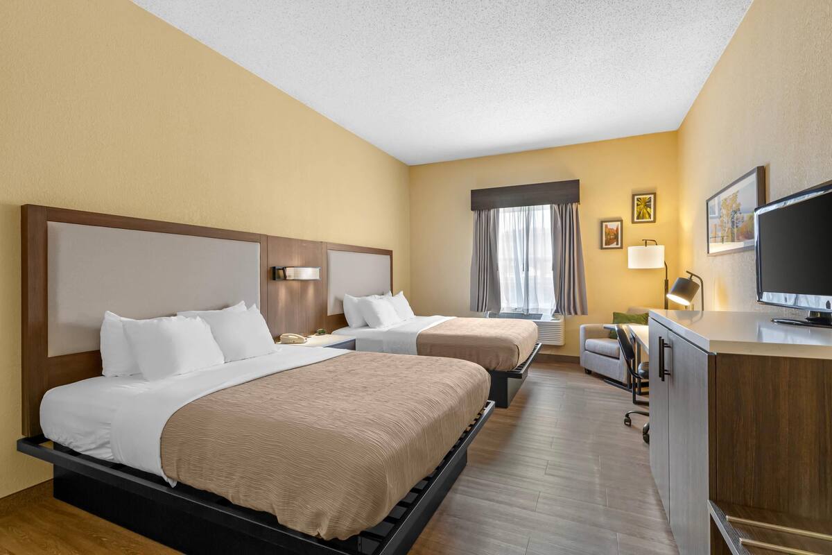 A hotel room with two beds, a desk, a television, and a window with curtains.