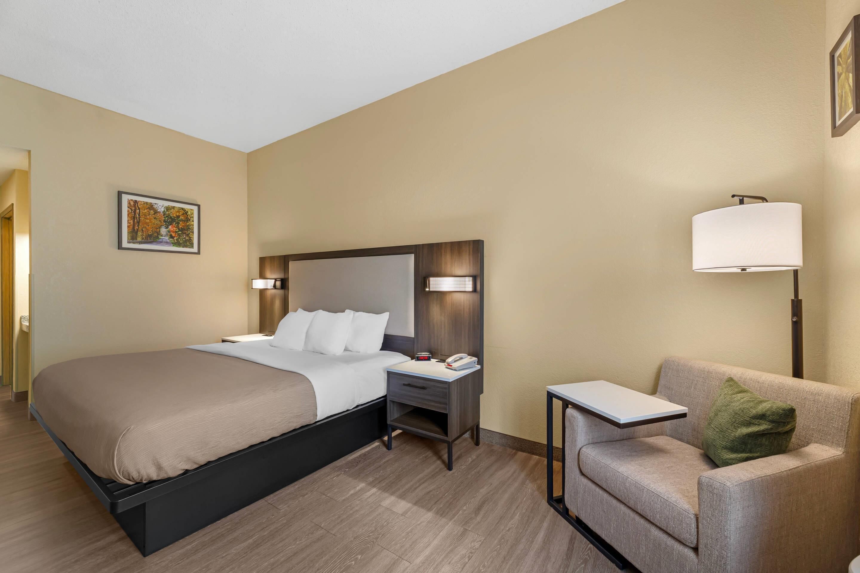 Una habitación de hotel con cama, mesita de noche, lámpara y una silla.